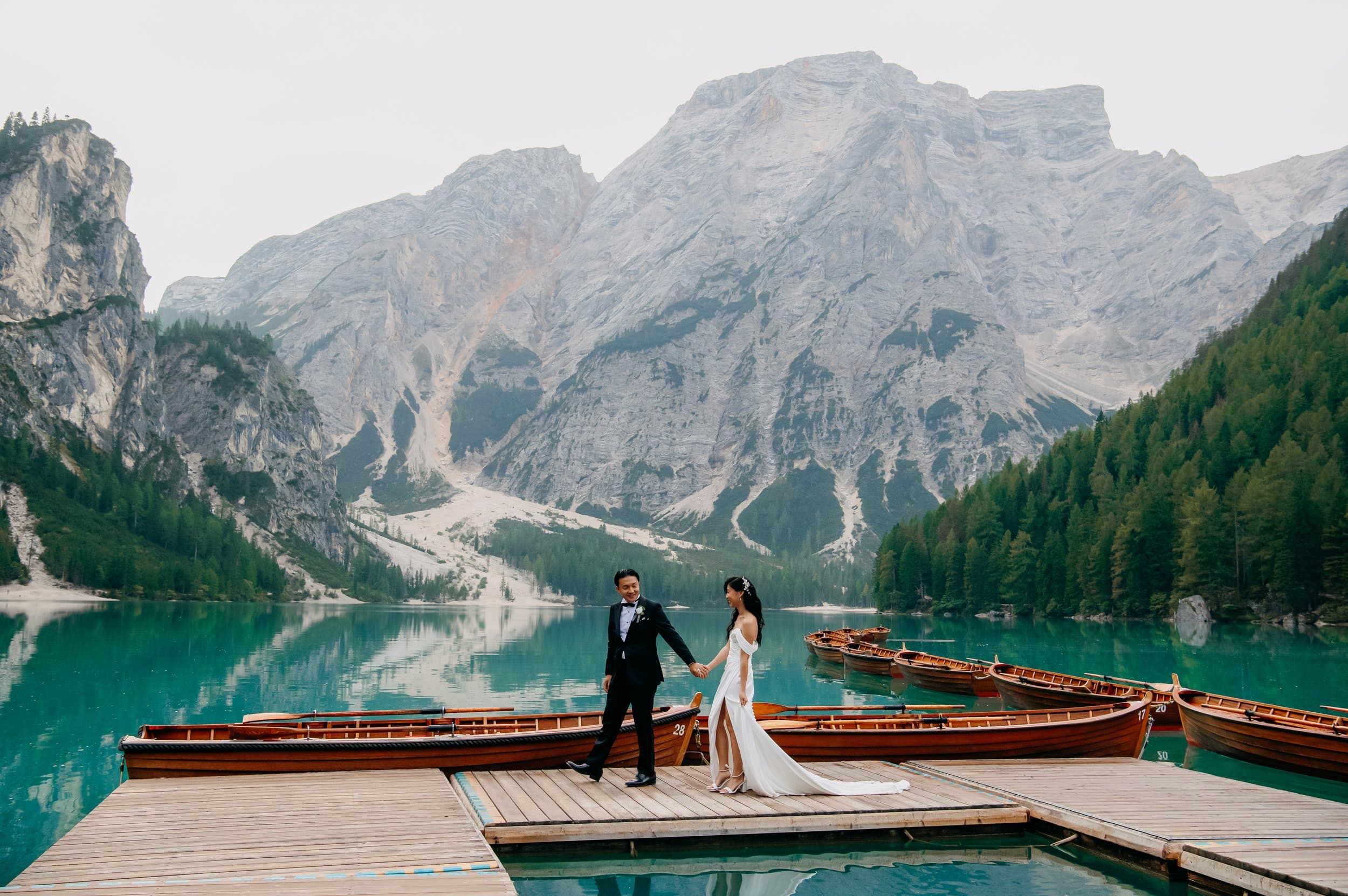 Lago di Braies wedding photographer: couple on the wooden jetty beside moored rowing boats and the turquoise lake