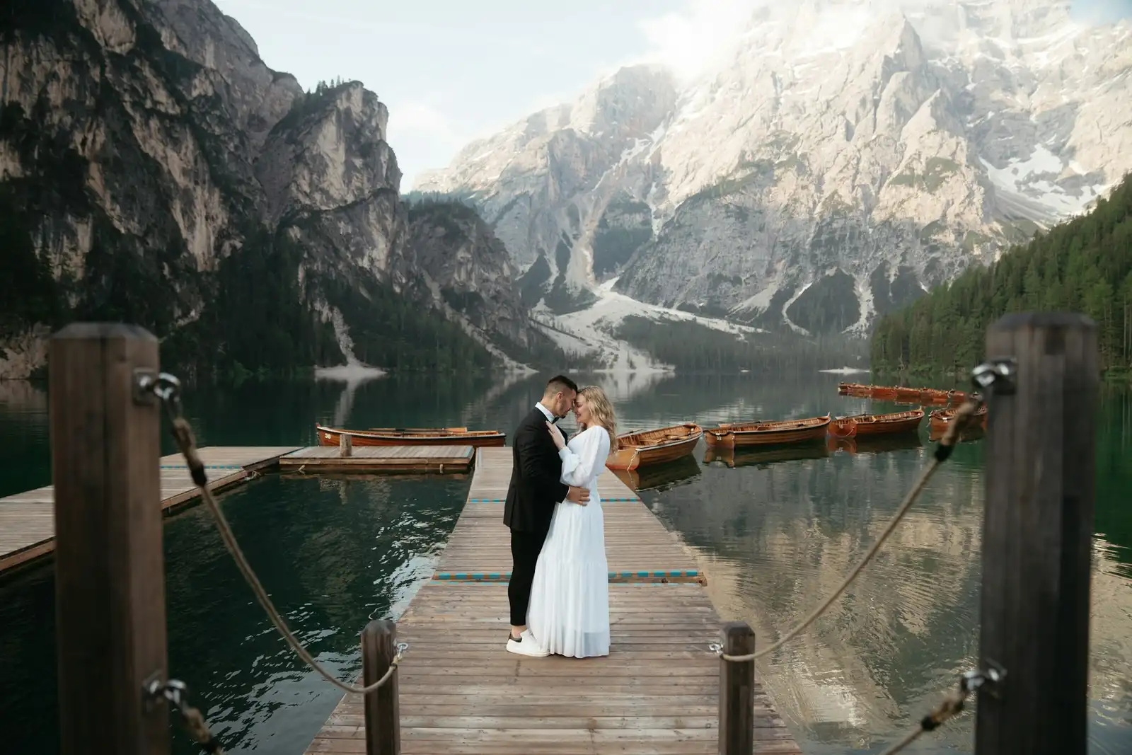 The Ultimate Guide to Eloping at Lake Braies: Logistics, Permits & Best Times Couple embracing at the end of a wooden dock on Lago di Braies, boats and Dolomites behind