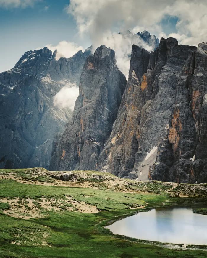 Prato Piazza: The Quiet Alternative to Lake Braies for Your Elopement Green alpine meadow with a small tarn below sheer Dolomites rock walls and drifting cloud