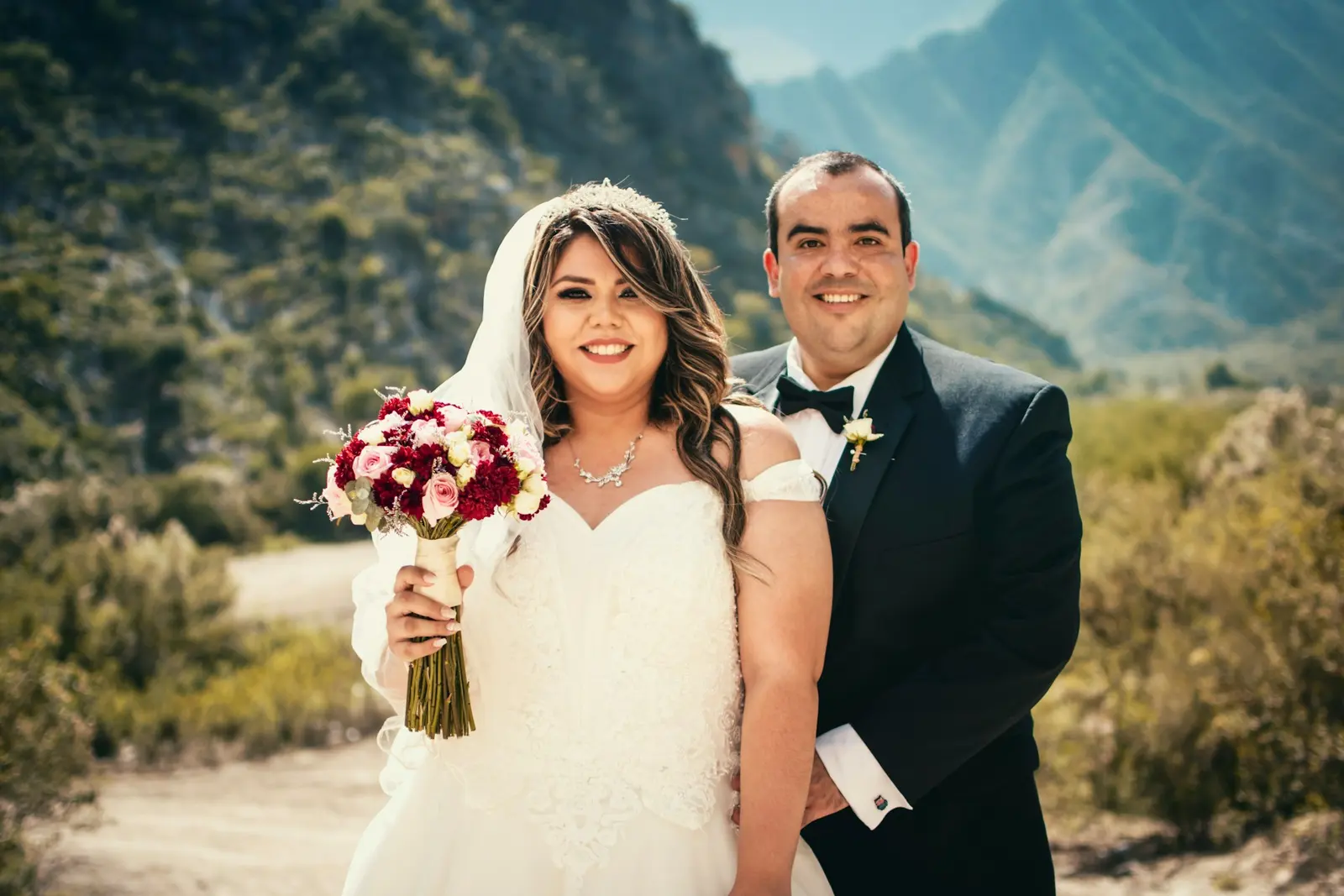 Planning a Vow Renewal or Anniversary Session in the Dolomites Smiling couple posing with a red bouquet, hills softly blurred behind them
