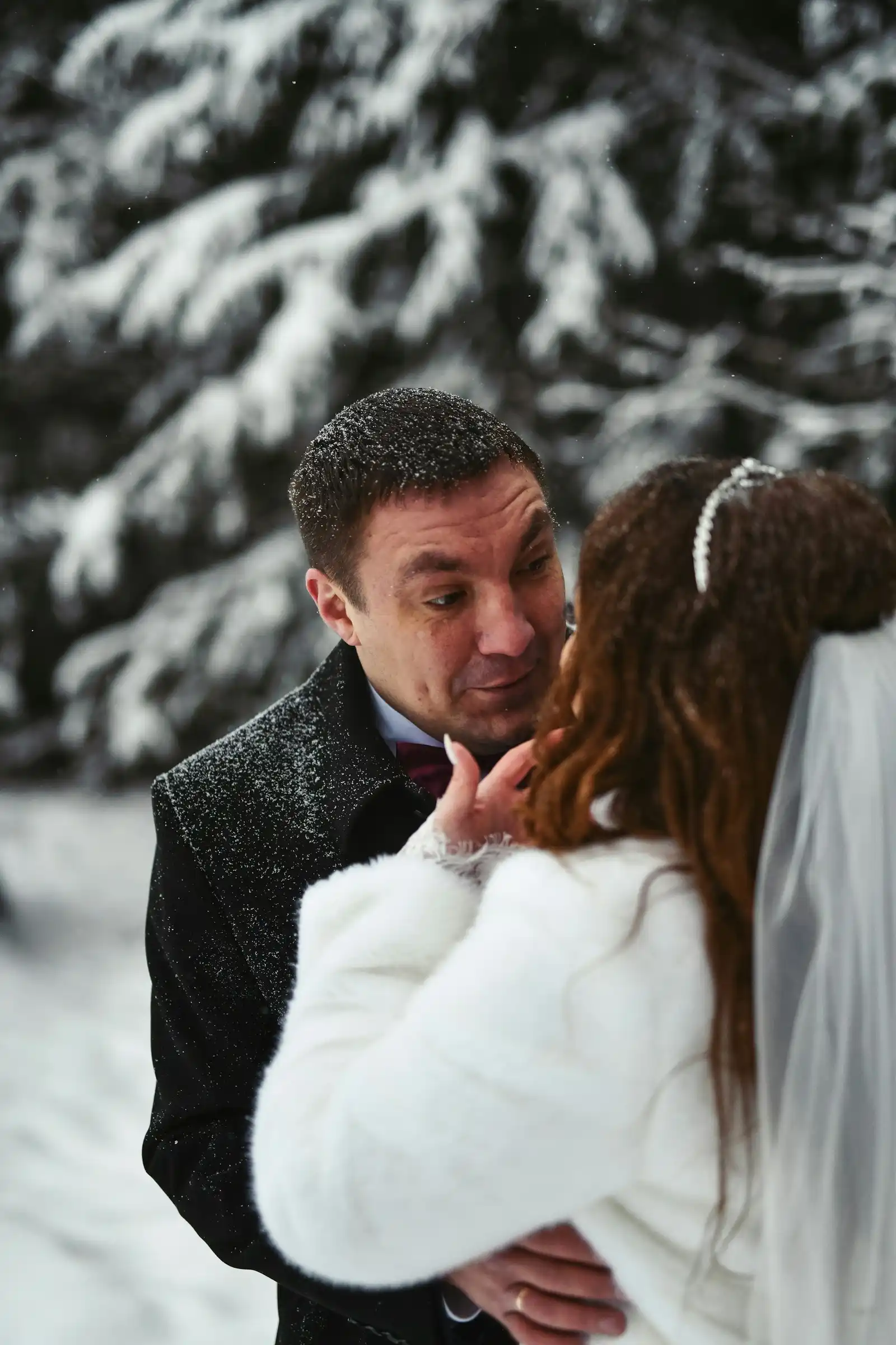 Winter Elopement at Lago di Braies: What to Expect Bride and groom sharing a close embrace in the falling snow beside snow-laden pines